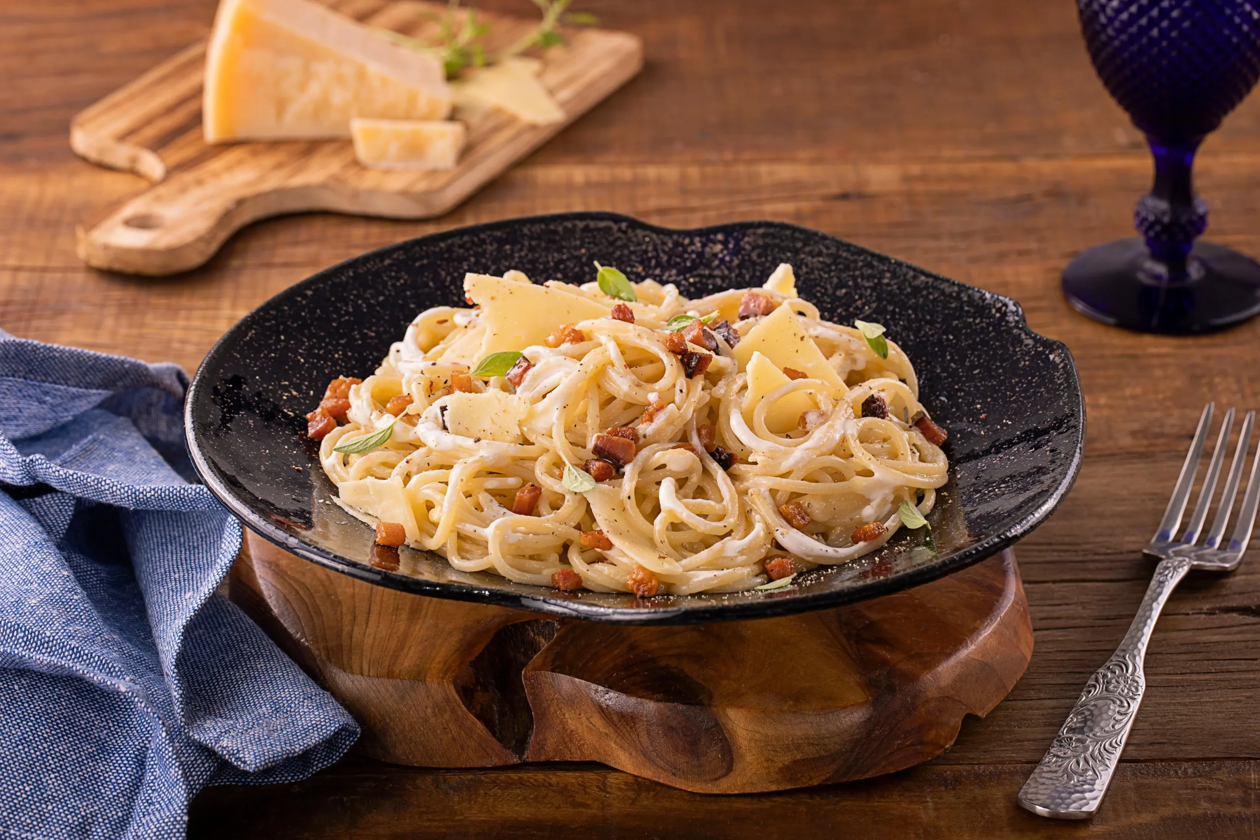 Na imagem, há um prato preto com macarrão á carbonara