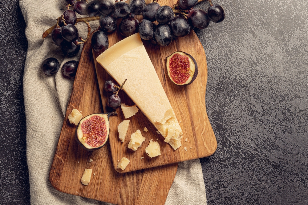 Queijo parmigiano reggiano cortado em tábua ao lado de uvas