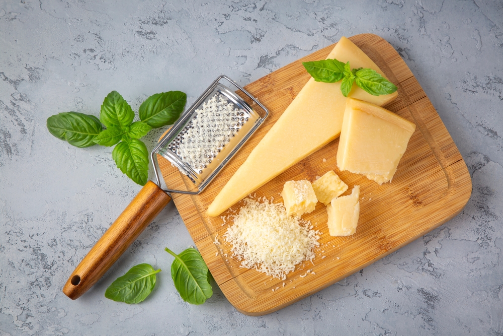 Queijo parmesão em peça e ralado em tábua de madeira