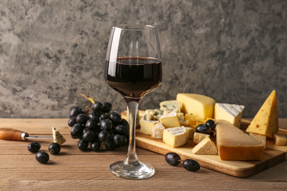 Taça de vinho tinto ao lado de uvas e pedaços de queijos