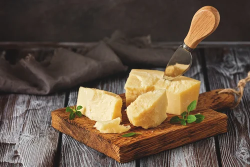 Na imagem, há diversos pedaços de queijo parmesão em tábua de madeira