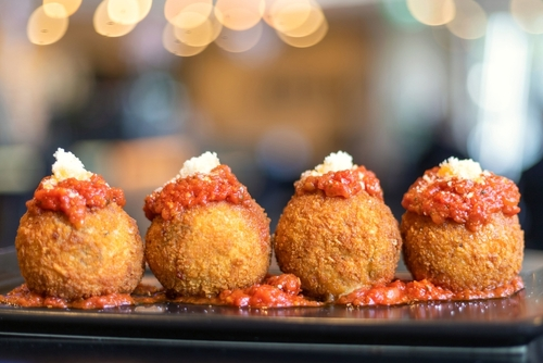 Na imagem, há quatro arancini bolinhos de arroz em uma mesa